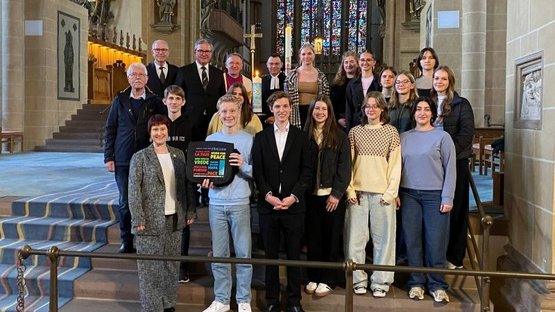 Das Foto zeigt die handelnden Akteure vor der Friedenskerze nach dem Gottesdienst im Altarraum des Domes zu Paderborn. Die Schülerinnen und Schüler des Gymnasiums St. Michael mit ihrer Lehrerin Manuela Lüftner, Christine Bentler (2. Stellv. Vorsitzende des Kreisverbandes Paderborn im Volksbund), Hermann-Josef Bentler (Mitglied des Kreisvorstandes Paderborn im Volksbund), Manfred Müller (Landrat a.D. und ehemaliger Vorsitzender des Kreisverbandes Paderborn im Volksbund), Bürgermeister Michael Dreier, Dechant Benedikt Fischer und Pfarrer Dr. Eckhard Düker ( v.u. nach o.).